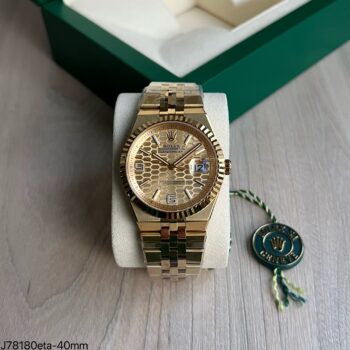 Super clone Rolex Land Dweller ETA 40mm com mostrador honeycomb champagne dourado, bezel fluted canelado e pulseira jubilee full gold, sobre suporte branco com caixa verde Rolex ao fundo
